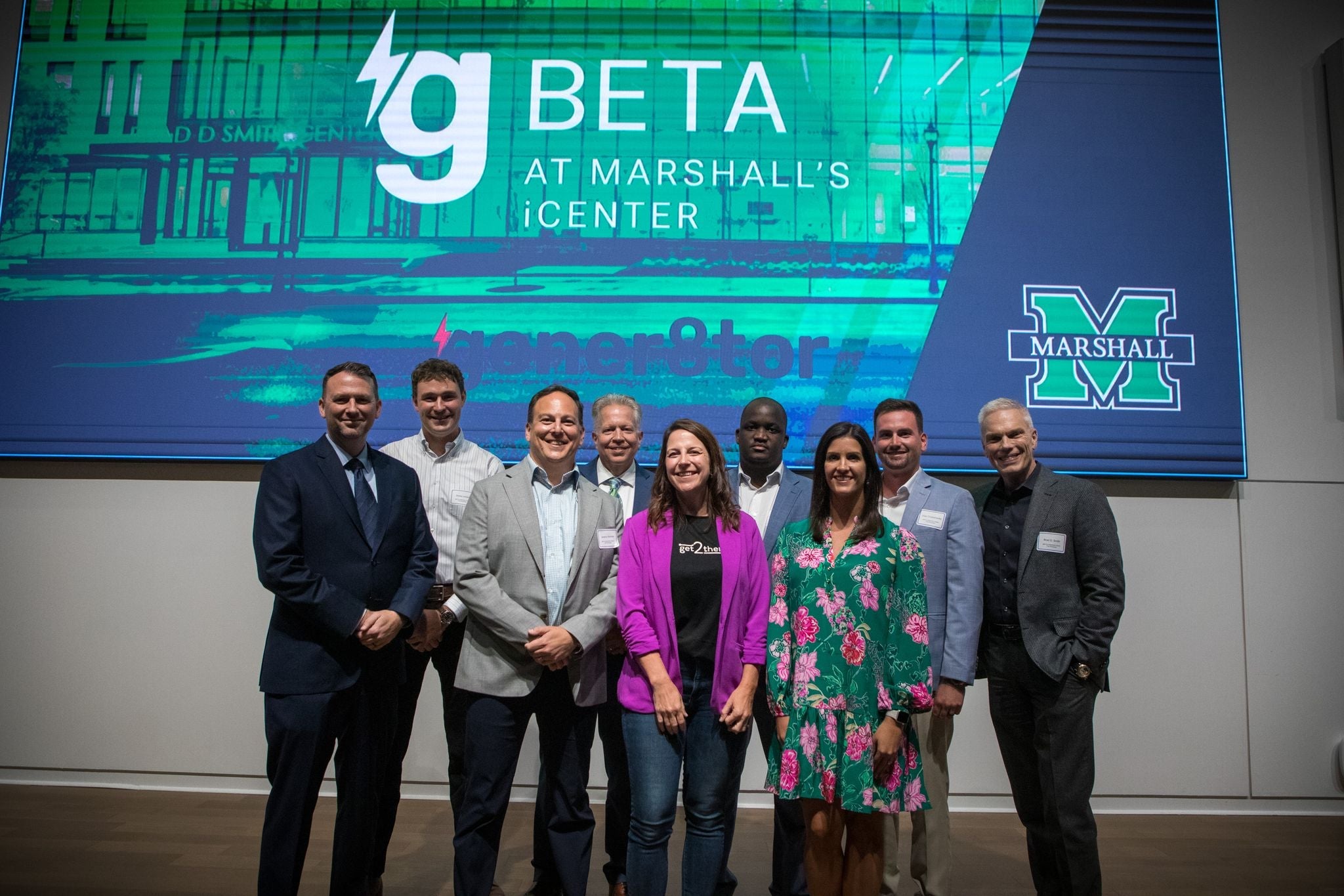 Group photo of gBETA at Marshall’s iCenter program participants and partners standing in front of a presentation screen displaying the gBETA and Marshall University logos.