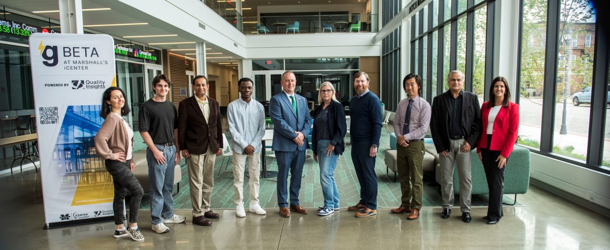 Participants in the gBETA at Marshall's iCenter program pose for a group photo beside a gBETA banner inside the iCenter lobby. The group stands in front of a seating area and large windows in the modern facility.