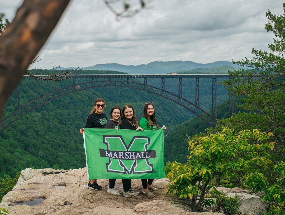 Students smile with a Marshall Flag with the New River Gorge Bridge in the background