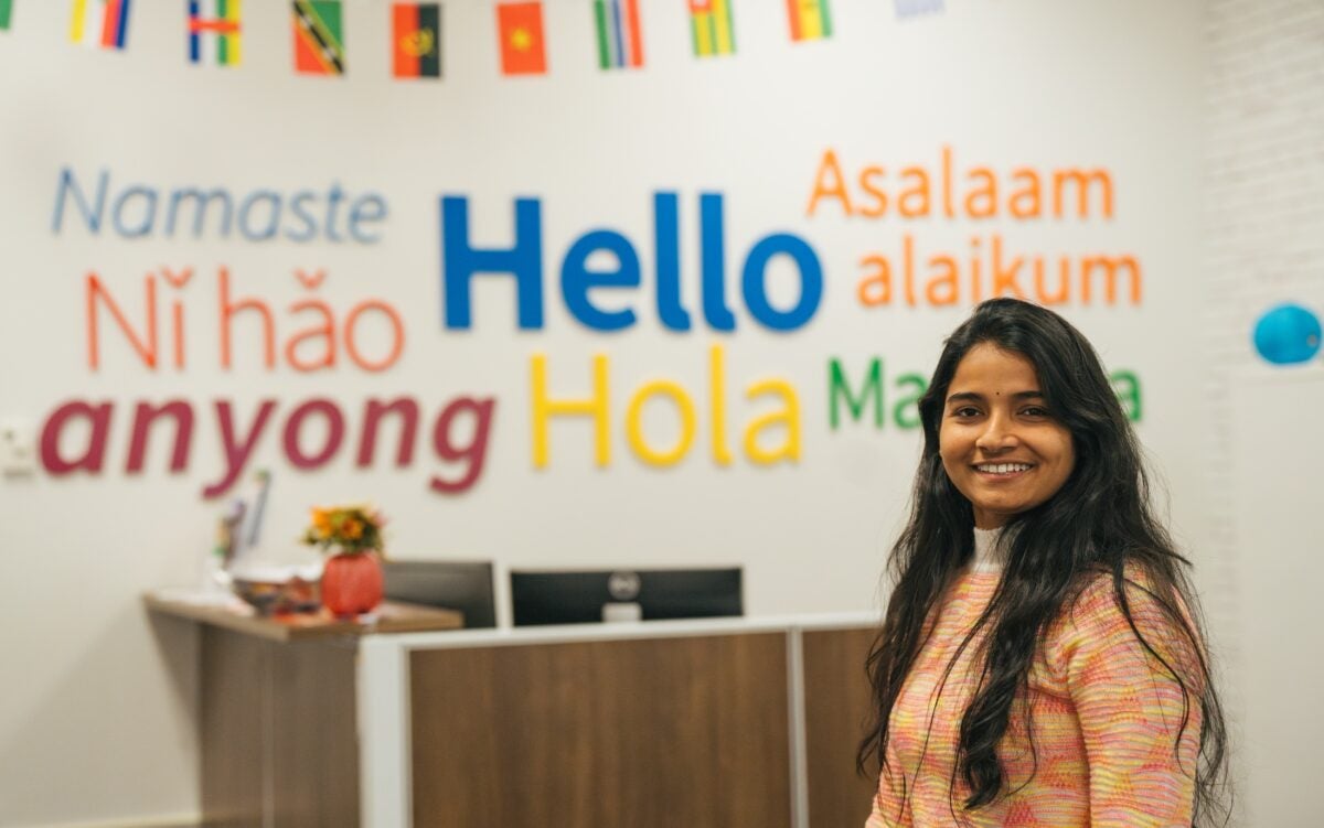 student smiling in front of a sign saying hello in several different lanaguages