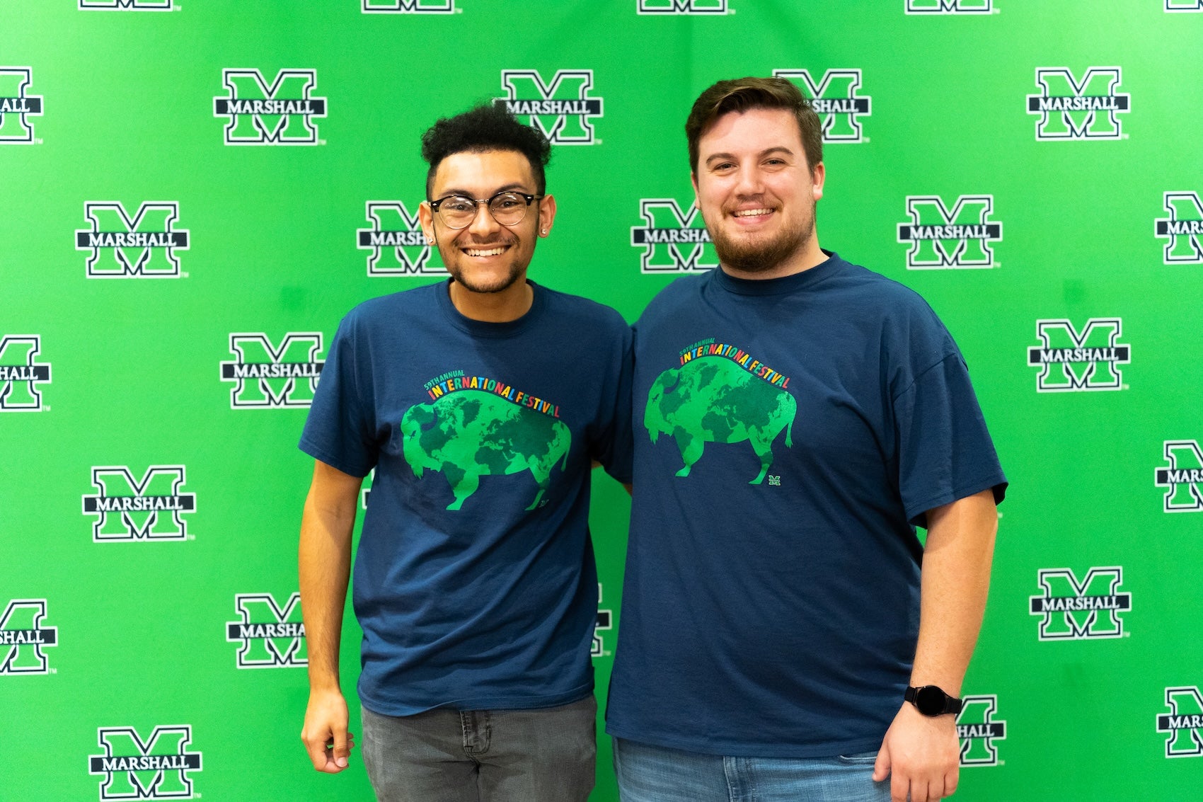 two students in Marshall shirts smiling at the camera in front of a green background