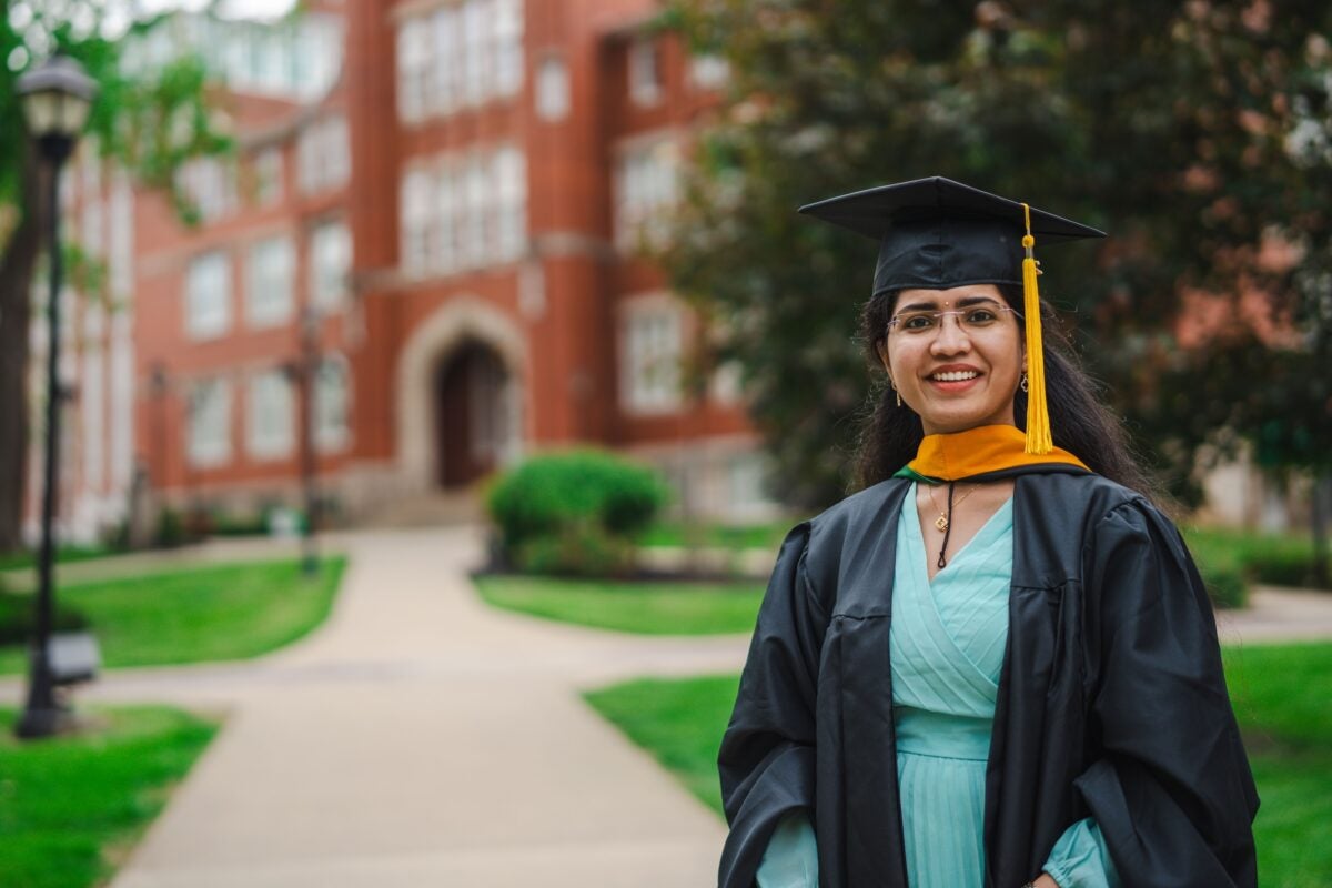 international student in cap and gown in front of Old Main