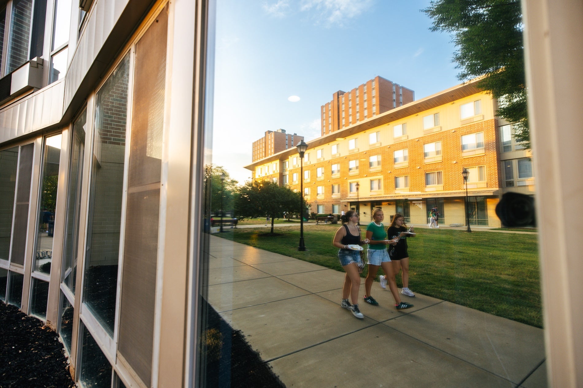 reflection in a residence hall window of students walking across campus