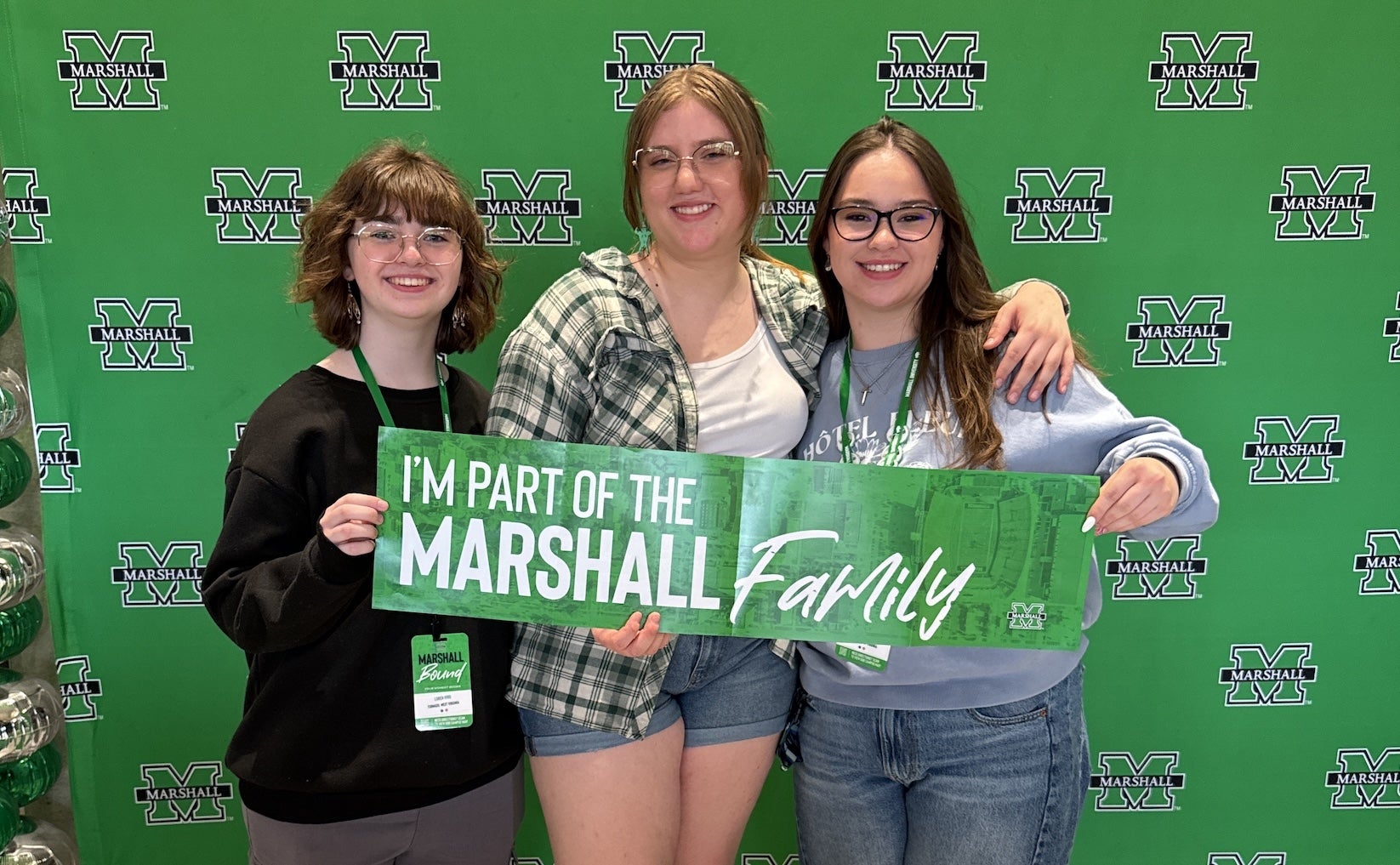 three students standing in front of a Marshall background holding a sign reading "I'm part of the Marshall family"