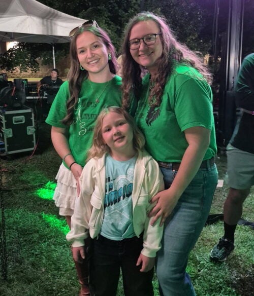 Three sisters smile together while wearing Marshall University shirts