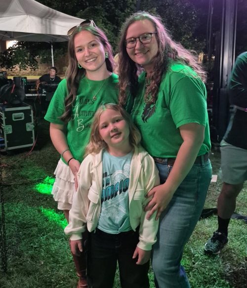 Three sisters smile together while wearing Marshall University shirts