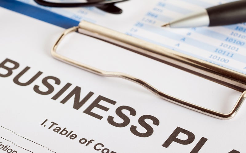 A clipboard shows a paper with the headline Business Plan at the top