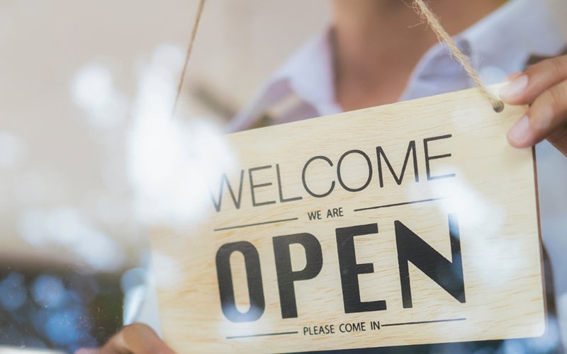 A person hanging an open sign in a window