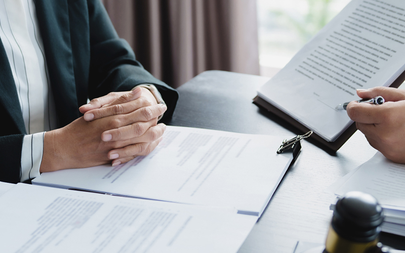 A person sitting at a desk with their hands folded on a folder of legal papers