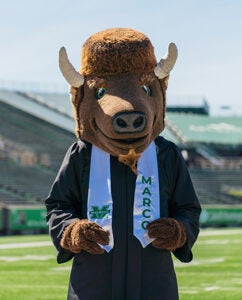 Marco stands in the middle of Joan C. Edwards stadium wearing his graduation cap and MARCO stole.