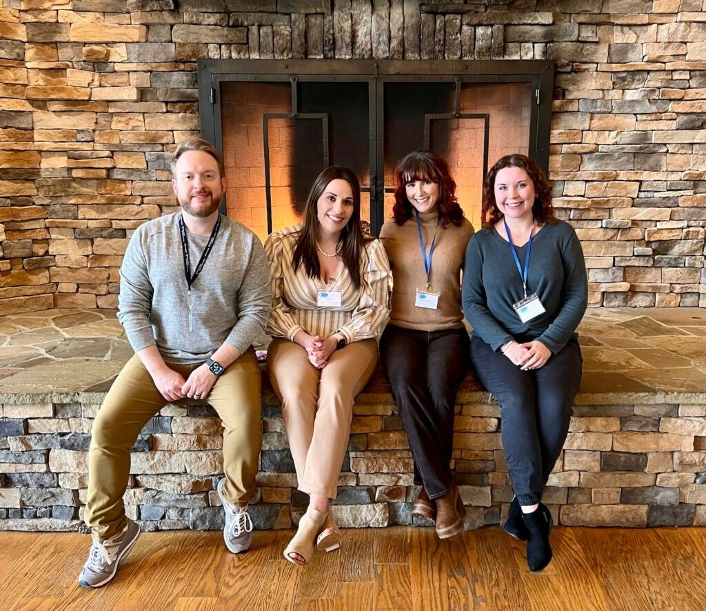 Nate Hensley, Sarah Frye, Shelby Babbington and Nakayla Elliott sitting in front of a fireplace and smiling