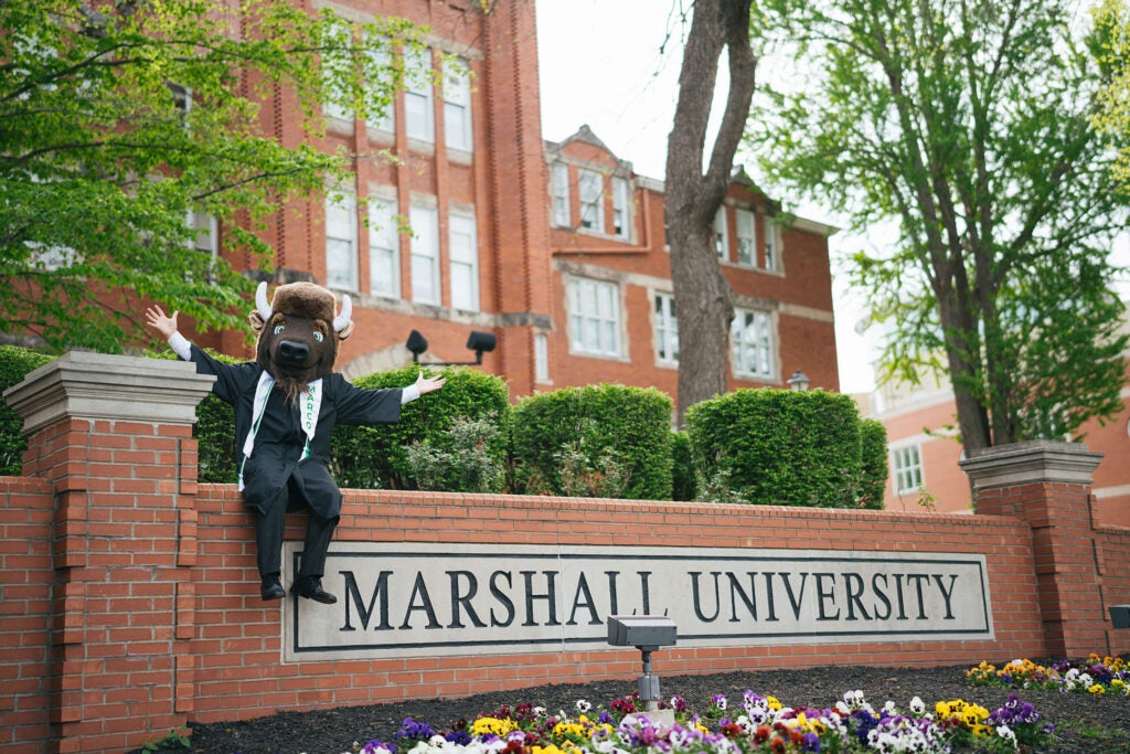 Marco wears his graduation gown and poses for a photo outside of Marshall University's Old Main