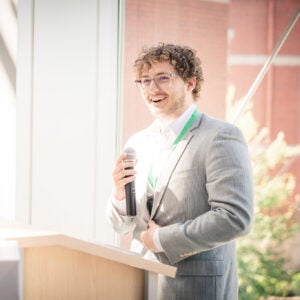 Luke Jeffery stands at a podium with a microphone addressing his class of Yeager Scholars