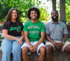 Tristan and his parents, all wearing Marshall attire, smile together on Marshall's Huntington Campus