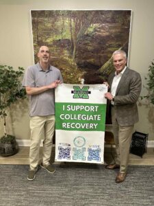 Jeremy Bailey and President Brad D. Smith hold a Collegiate Recovery banner in the President's Office at Marshall University 