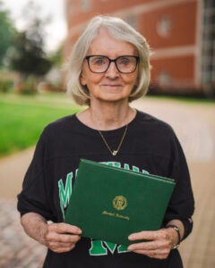 Margaret Wright Miller wears a Marshall University shirt and proudly holds her diploma on Marshall's Huntington campus