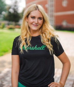 Sydney Barbour wears a black Marshall University shirt while smiling on Marshall's Huntington campus