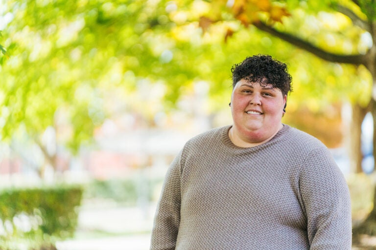 Marshall student, Mika Sheppard smiles at the camera standing outside in front of fall trees