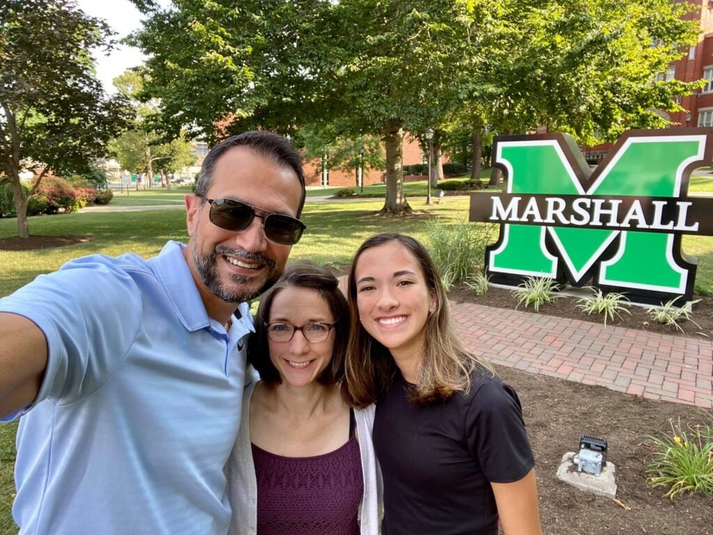 Dr. Dru Bora, Dr. Kim DeTardo-Bora and Asha Bora smile together in front of a Marshall sign