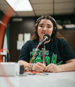 Emma Johnson wears headphones and speaks into a microphone in Marshall University's WMUL radio studio. 