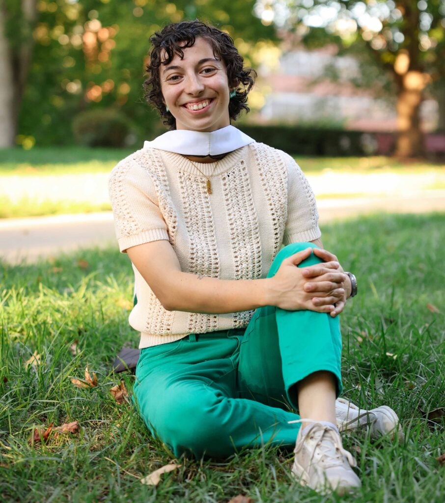 Michaela Marshall sits in the grass wearing her graduation hood