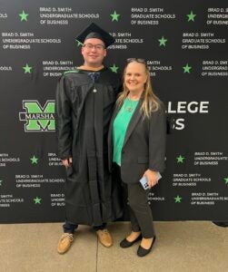 Ethan Starkey wears his cap and gown and smiles for a photo in front of a Marshall University background