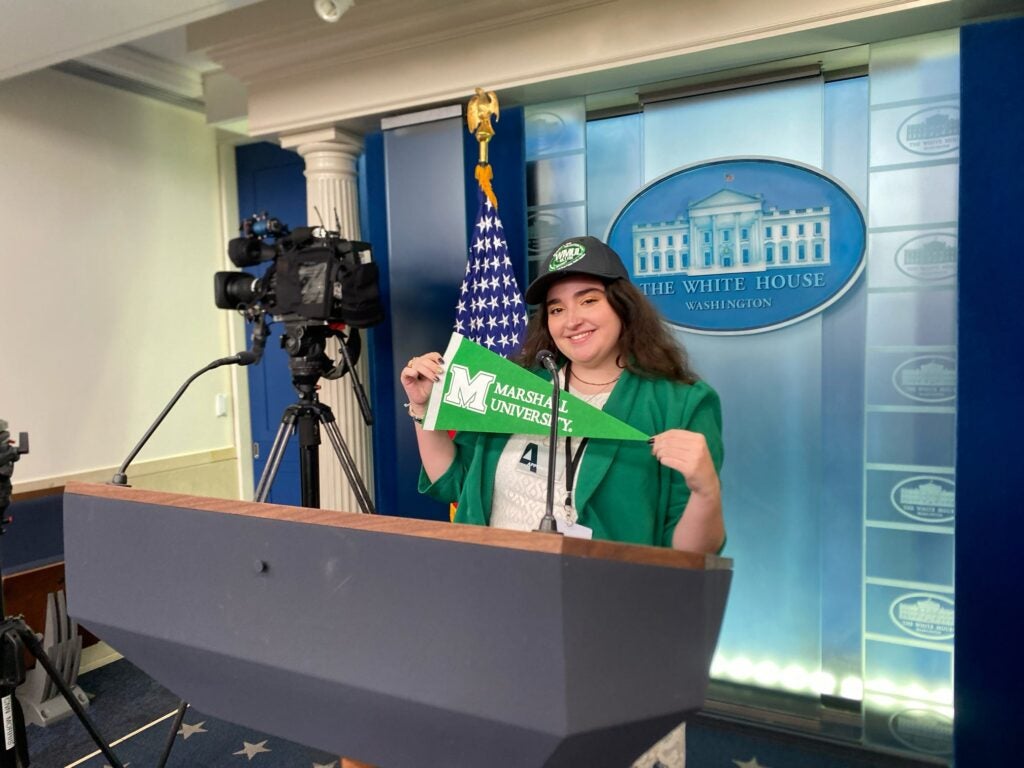 Emma Johnson stands at a podium in The White House holding a small Marshall pennant.