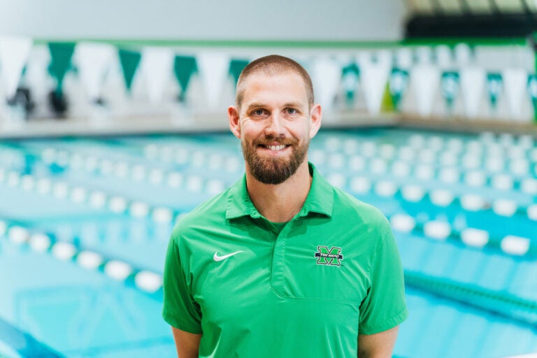 Ian Walsh, Head Coach of Marshall Swimming and Diving, smiles at the camera while standing in front of the pool.