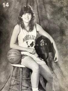 Lea Ann Parsley-Davenport holds a fire helmet and leans on a basketball for a Marshall Women's Basketball media photo in 1989