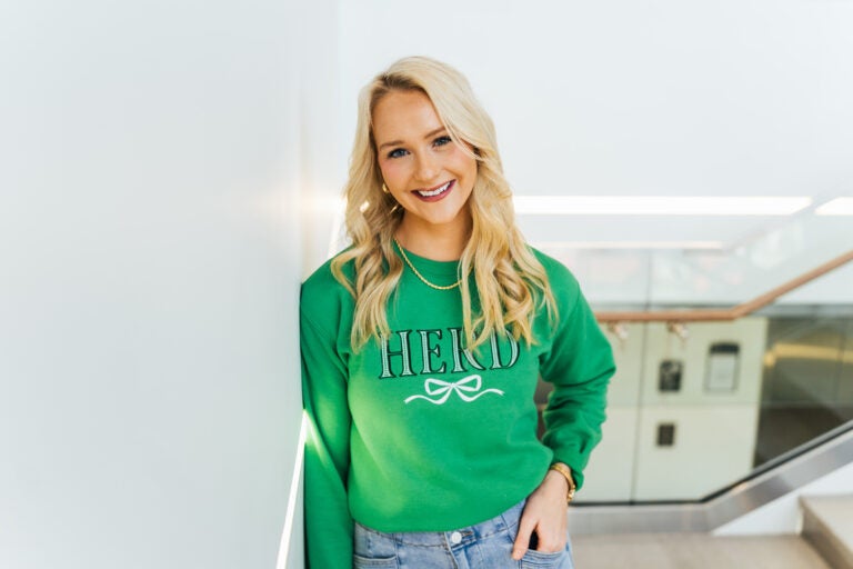 Bethany Ledford wears a green Marshall University sweatshirt while leaning against a wall inside Marshall's Brad D. Smith Center for Business and Innovation.
