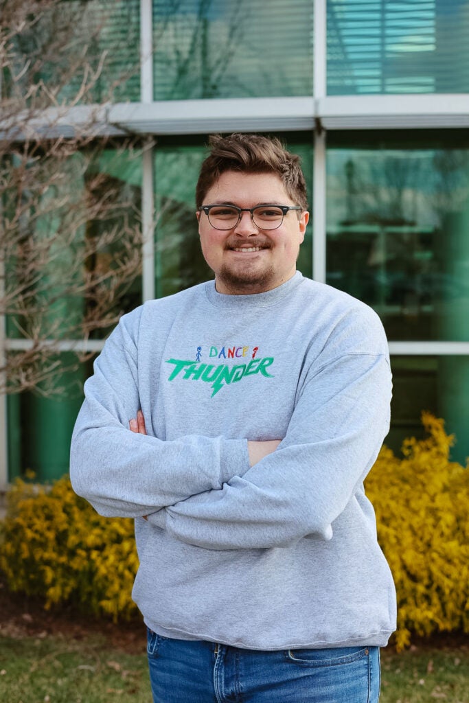 Braden Cotton smiles with his arms crossed while standing outside of Marshall University's Harless Dining Hall