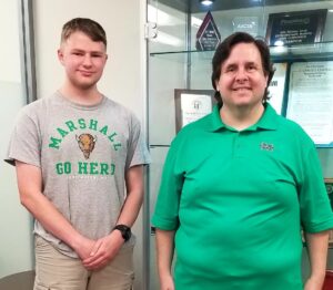 Jamison Lewis and Glen Glen Midkiff wear Marshall attire and smile together in front of an award case in the College of Business