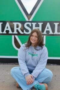 Emily Price sits smiling in front of a large Marshall sign