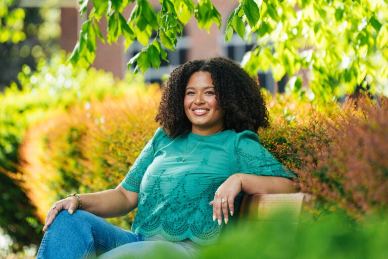 Haleigh Muncy smiles while sitting on a bench surrounded by lush plants