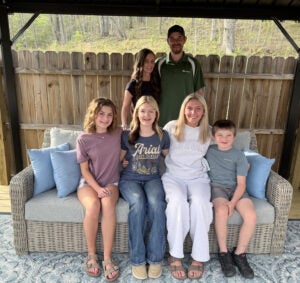 Brandon Adams stands with his wife while their children sit in front of them. 