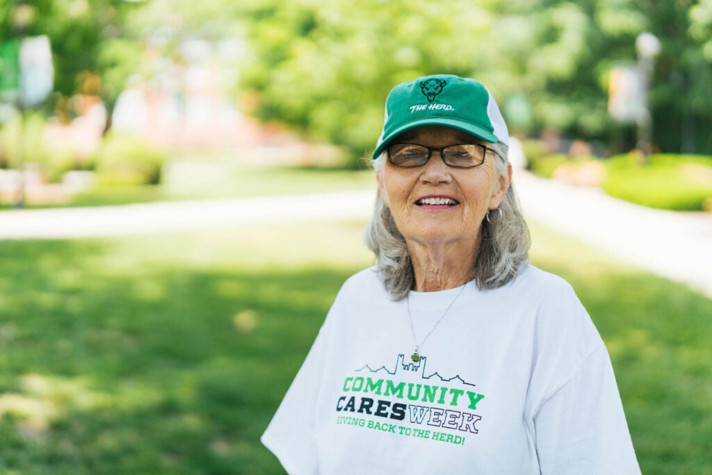 Marshall University alumna Sandra Morris smiles for a photo in her Community Cares Week t-shirt and a Marshall hat