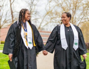 Markayla Moore and Toni Wooding smile and hold hands while looking at each other in their graduation regalia