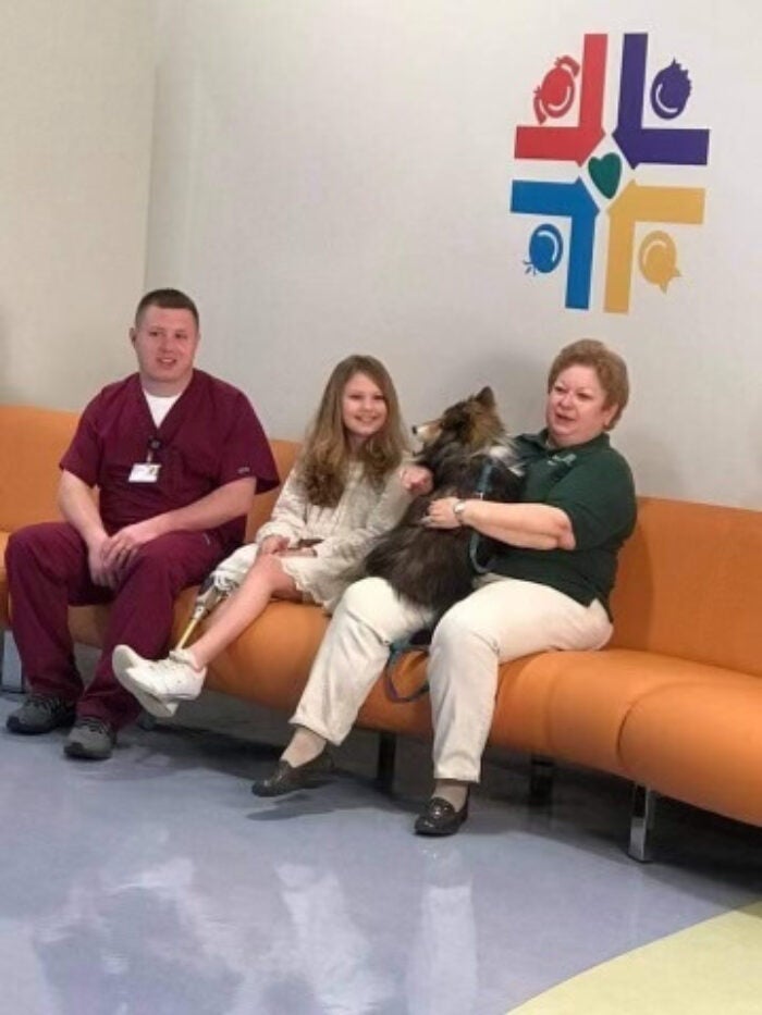 Bella and Angel visit with a young patient and family members in a hospital waiting area.