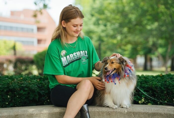 Marshall student Isabella sits outdoors with therapy dog Bella on campus.