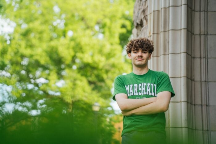 Mark Hysell wears a Marshall t-shirt and stands with his arms crossed in front of a stone building.