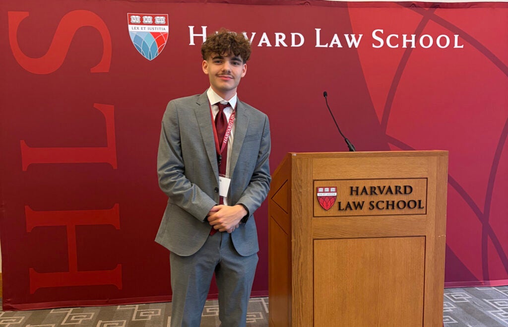 Mark Hysell wears a suit and smiles next to a Harvard Law School podium in front of a Harvard backdrop