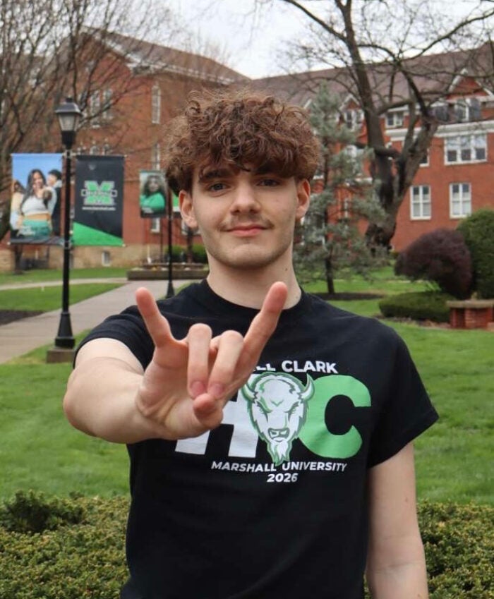 Mark Hysell wears a black Marshall t-shirt and smiles with Marshall banners and building in the background