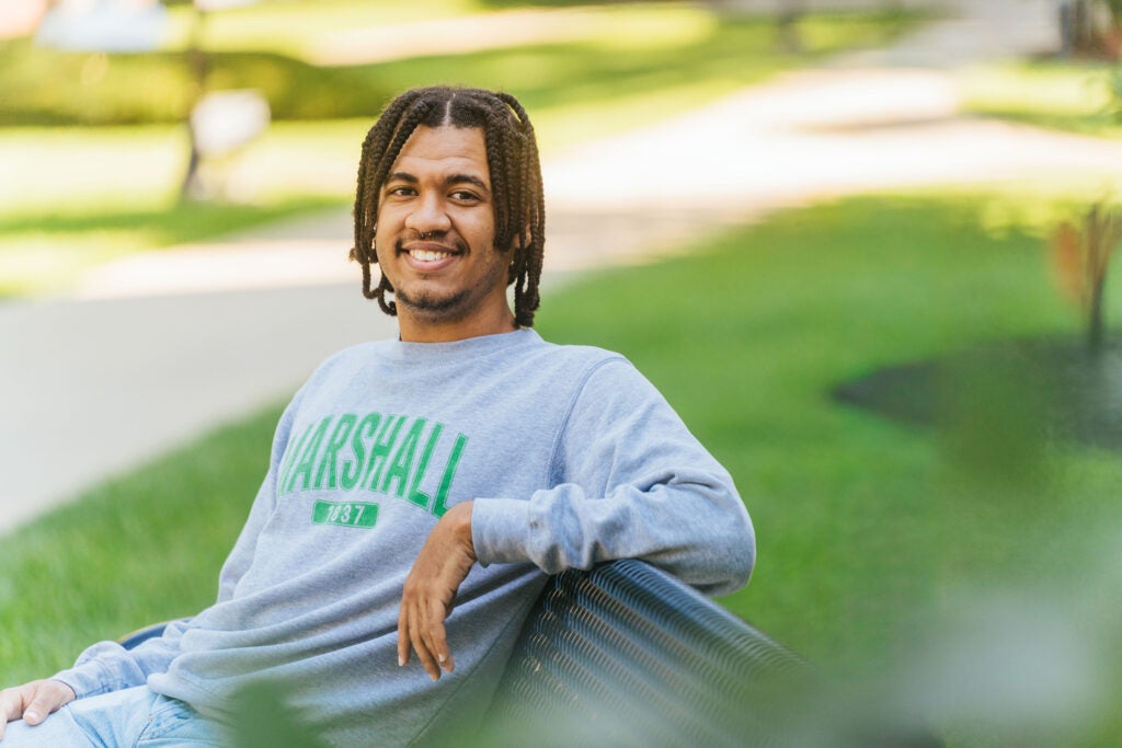 Kameron Riggins smiles while sitting on a bench on Marshall's Huntington campus