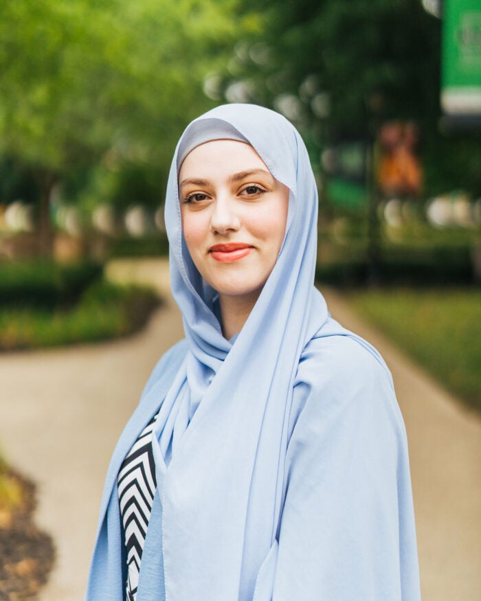 Hind Jamal wears a light blue hijab smiles while standing outdoors on Marshall University’s campus.