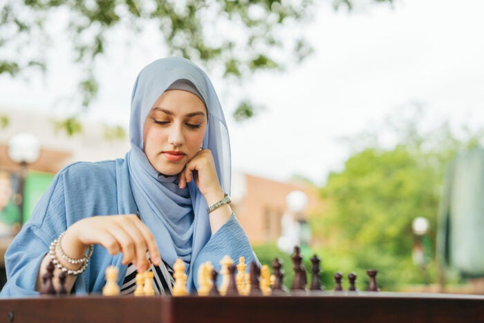 Hind Jamal wears a light blue hijab thoughtfully considers her next move while playing chess at an outdoor table on Marshall University’s campus.