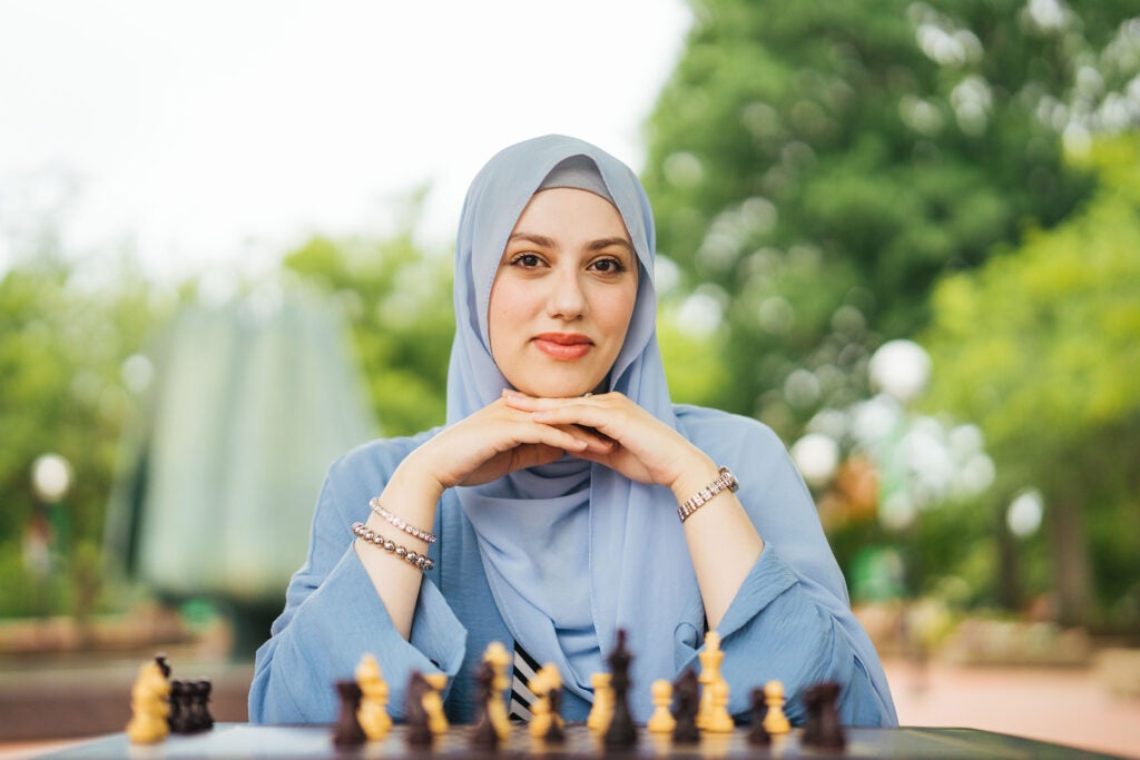 Marshall University graduate student Hind Jamal wears a light blue hijab while sitting behind a chessboard on Marshall University’s Memorial Plaza.