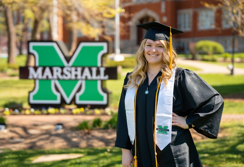 Taya Horob in her cap and gown in front of a Marshall University sign