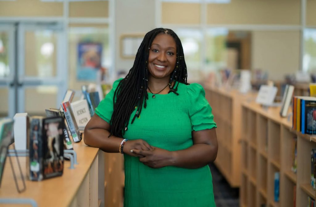 Cassie Owens Moore stands in a library smiling at the camera