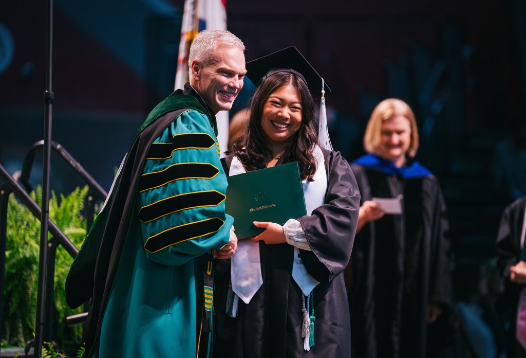 Gracie Queen holds her diploma cover and smiles with President Brad D. Smith during her Marshall University Commencement Ceremony