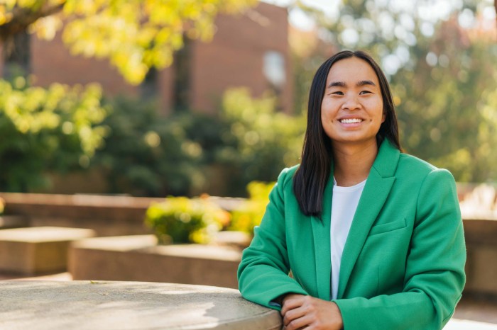 Hanna Shrout wears a green blazer and sits at an outdoor table on Marshall University's campus